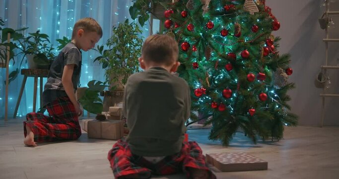 two children running towards their presents on Christmas morning. Two boys in pajamas running to look at the gifts under the Christmas tree.