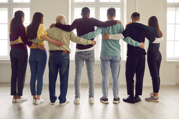 Team of confident diverse people standing, looking out window together and hugging ready to always support each other. Group of mixed-race friends or colleagues showing unity and mutual responsibility - obrazy, fototapety, plakaty