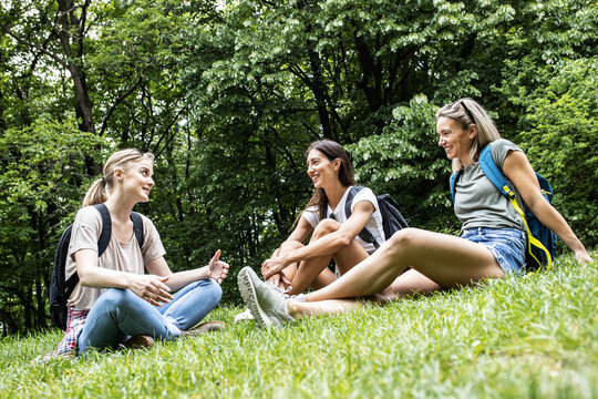 Group of female hikers taking a break after long walk in nature.They sitting on grass and making fun.