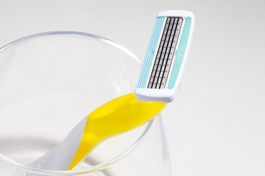 Yellow razor with four blades for women shaving in a glass glass on a neutral background