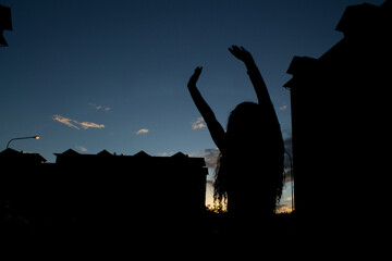 silhouettes of a girl among houses outdoors at sunset