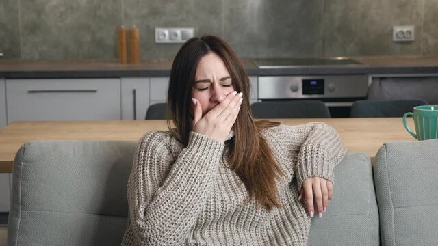 Medium shot of young woman stretching his arms and yawn sitting in couch in the kitchen