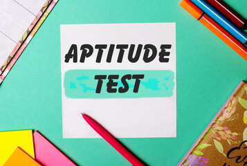 APTITUDE TEST written on a turquoise background near bright stickers, notepads and markers