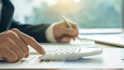 Accountants press the calculator placed on the graph to make monthly financial report or company profit at the bookkeeper desk.