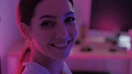 Attractive portrait of young elegant woman. Young millennial female smilling and look at camera, playfully posing for camera on the pink and blue neon lights in slow motion. - Powered by Adobe