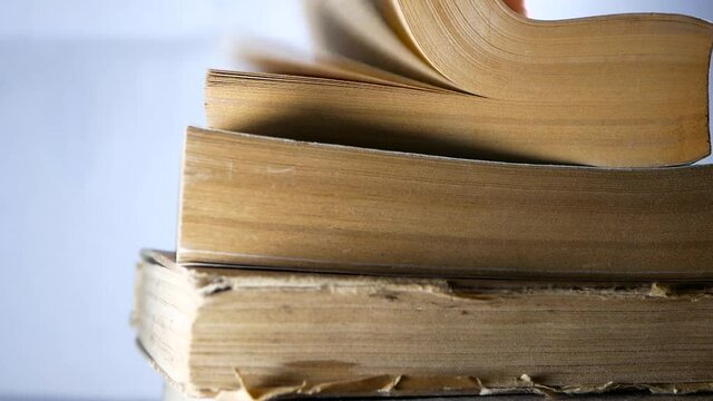 Stack of old aged books, man hand turning the book pages in slow motion.