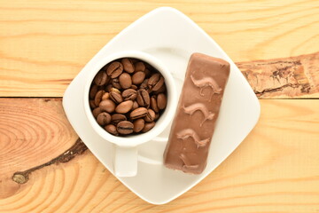 One chocolate energy bar, cup and saucer with coffee beans, close-up, on a wooden table.