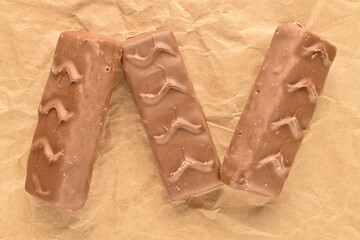 Three chocolate bars with nuts, close-up, on brown paper.