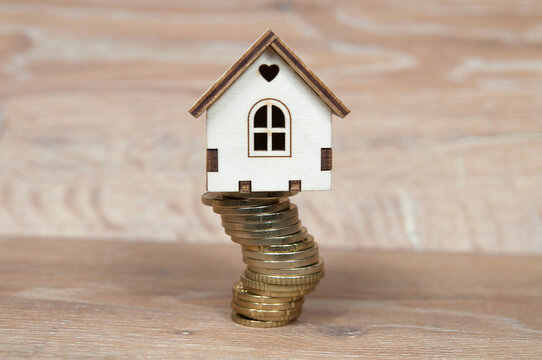 wooden house on a stack of coins folded crookedly, real estate insurance concept