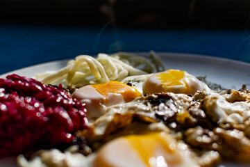 Fried eggs with mushrooms, long cheese noodles and beetroot caviar, a hearty fried dish for Breakfast with appetizers. The flowing liquid yellow egg yolk
