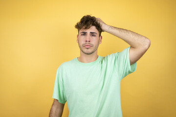 Handsome man wearing a green casual t-shirt over yellow background putting one hand on his head...