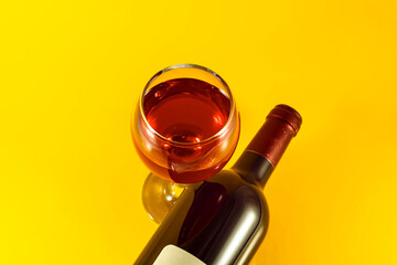 Bottle and glass of red wine on a yellow background.