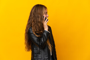 Child over isolated yellow background keeping a conversation with the mobile phone with someone