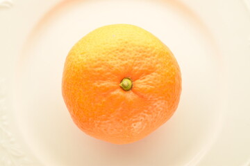 One organic yellow tangerine, close-up, on a ceramic white plate.