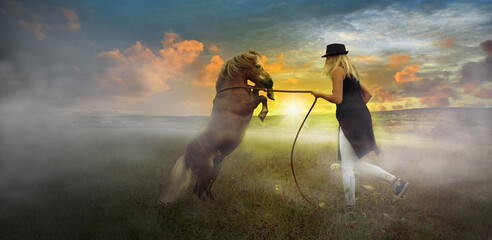 Young woman rider training with her pony horse, stallion climbing on 2 hooves in the evening with...