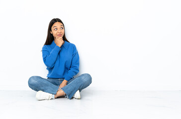 Young mixed race woman sitting on the floor isolated on white background thinking an idea while looking up