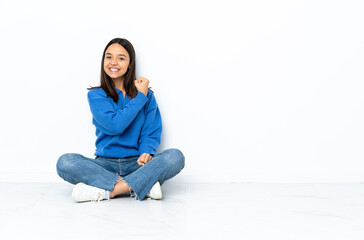 Young mixed race woman sitting on the floor isolated on white background celebrating a victory