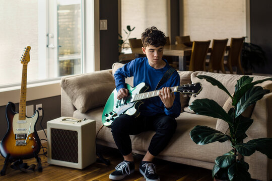 Young male musician playing electric guitar at home