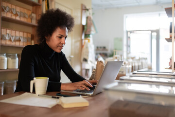 Smart black entrepreneur using laptop in shop