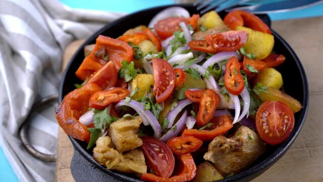 Cooked food in a frying pan. Meat with tomatoes, red pepper, onion, parsley and potatoes. Pork ojakhuri with vegetables. Georgian cuisine. Home menu. Modern Kitchen.