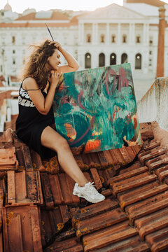 Female painter sitting on roof with abstract art canvas
