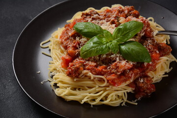 Plate of pasta Bolognese on dark background, Italian pasta spaghetti with roasted beef meat, tomato sauce, parmesan and basil.