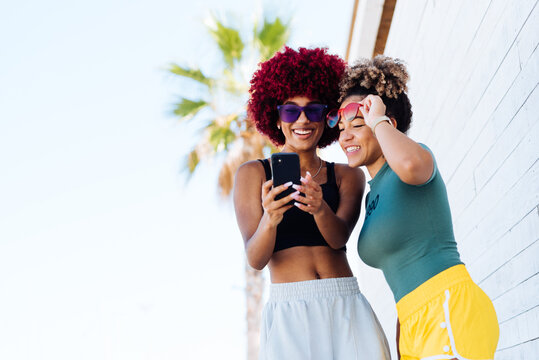 Two attractive latin girls with afro hair looking photos on cellphone.