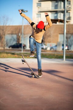 Young Caucasian teen with red hut jumping on a skateboard in the city
