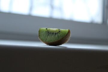 wedge slice of kiwi on a window sill white light background with a copyspace