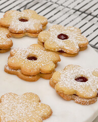 Flower shaped shortbread cookies filled with raspberry jam close up on cooling rack, vertical banner