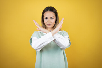 Pretty young woman standing over yellow background Rejection expression crossing arms doing negative sign, angry face