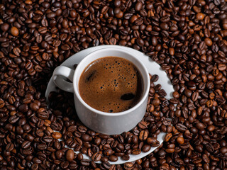 Close-up of a white espresso cup on a table with lots of coffee beans