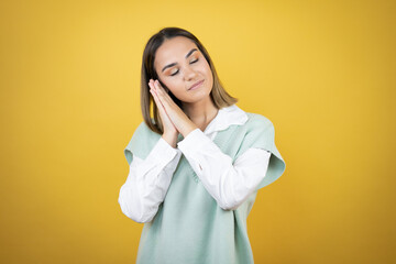 Pretty young woman standing over yellow background sleeping tired dreaming and posing with hands together while smiling with closed eyes.