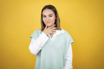 Pretty young woman standing over yellow background touching painful neck, sore throat for flu, clod and infection