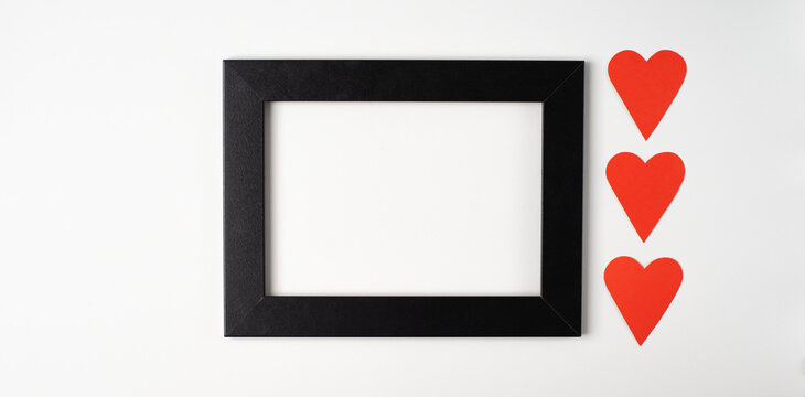 Black photo frame with red heart on the light (white) background. Valentine's Day concept. Flat lay, top view, space for text.