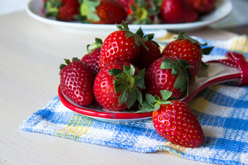 Strawberry background. A plate of fresh strawberries sits on a checkered tablecloth on a wooden table, copy space. Sweet, ripe strawberries. Harvest of organic local strawberries. Healthy food.