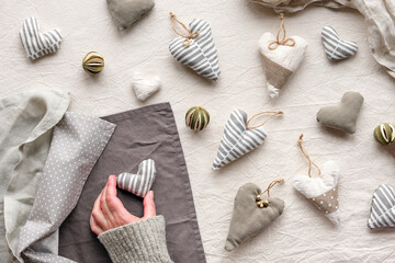 Hand made textile hearts and balls on cotton background. Textile stuffed toys, balls, towels in neutral colors. Hand hold soft heart. Monochromatic look, desaturated colors, grey winter window light.