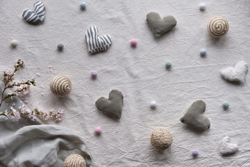 Fototapeta na wymiar Hand made linen hearts and balls on linen background. Textile handicraft in neutral colors. Springtime flower twigs. Hand hold soft heart. Monochromatic look, desaturated hues. Rustic seasonal decor.