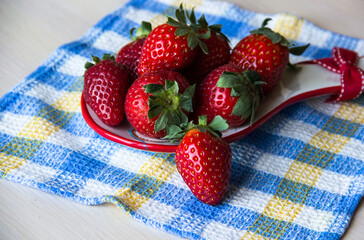Strawberry background. A plate of fresh strawberries sits on a checkered tablecloth on a wooden table, copy space. Sweet, ripe strawberries. Harvest of organic local strawberries. Healthy food.