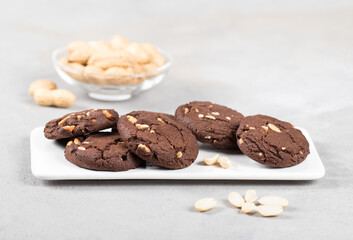 Vegan cocoa cookies with whole peanuts on a ceramic tray on a light background