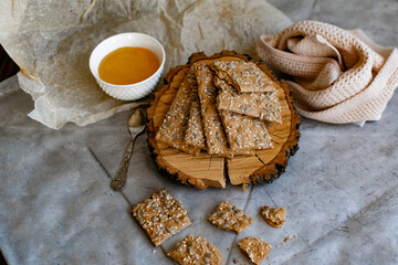 Healthy and nutritious diet bread with sesame and sunflower seeds on a thin crunchy malt base. Near natural bee honey and a wooden stand sawn