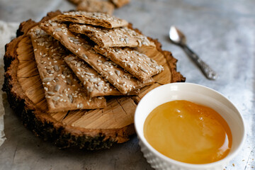 Healthy and nutritious diet bread with sesame and sunflower seeds on a thin crunchy malt base. Near natural bee honey and a wooden stand sawn
