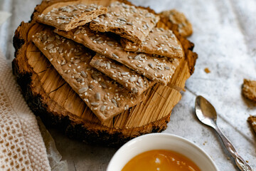 Healthy and nutritious diet bread with sesame and sunflower seeds on a thin crunchy malt base. Near natural bee honey and a wooden stand sawn