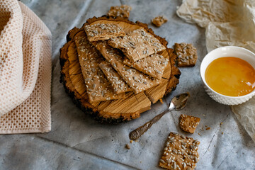 Healthy and nutritious diet bread with sesame and sunflower seeds on a thin crunchy malt base. Near natural bee honey and a wooden stand sawn