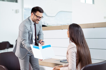 Salesman showing brochure to customer in car dealership showroom