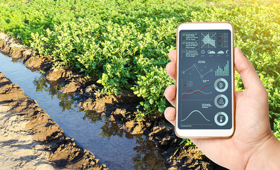 A farmer holds a phone with infographics in his hand against the background of a water filled...