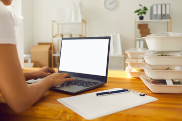 Over shoulder food and ready meal delivery worker or takeaway cafe employee working on laptop computer with blank mockup screen in office, processing orders from website or communicating with clients