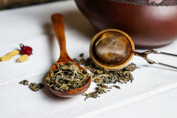 wooden spoon of dried green tea leaves on a wooden table on the background of a teapot and brewing...