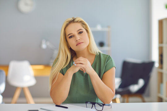 Supportive good-looking young woman sitting at desk attentively listening and looking at you. Video call or conference picture of professional trustworthy life coach or understanding psychologist