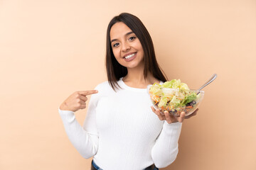 Young brunette girl holding a salad over isolated background proud and self-satisfied